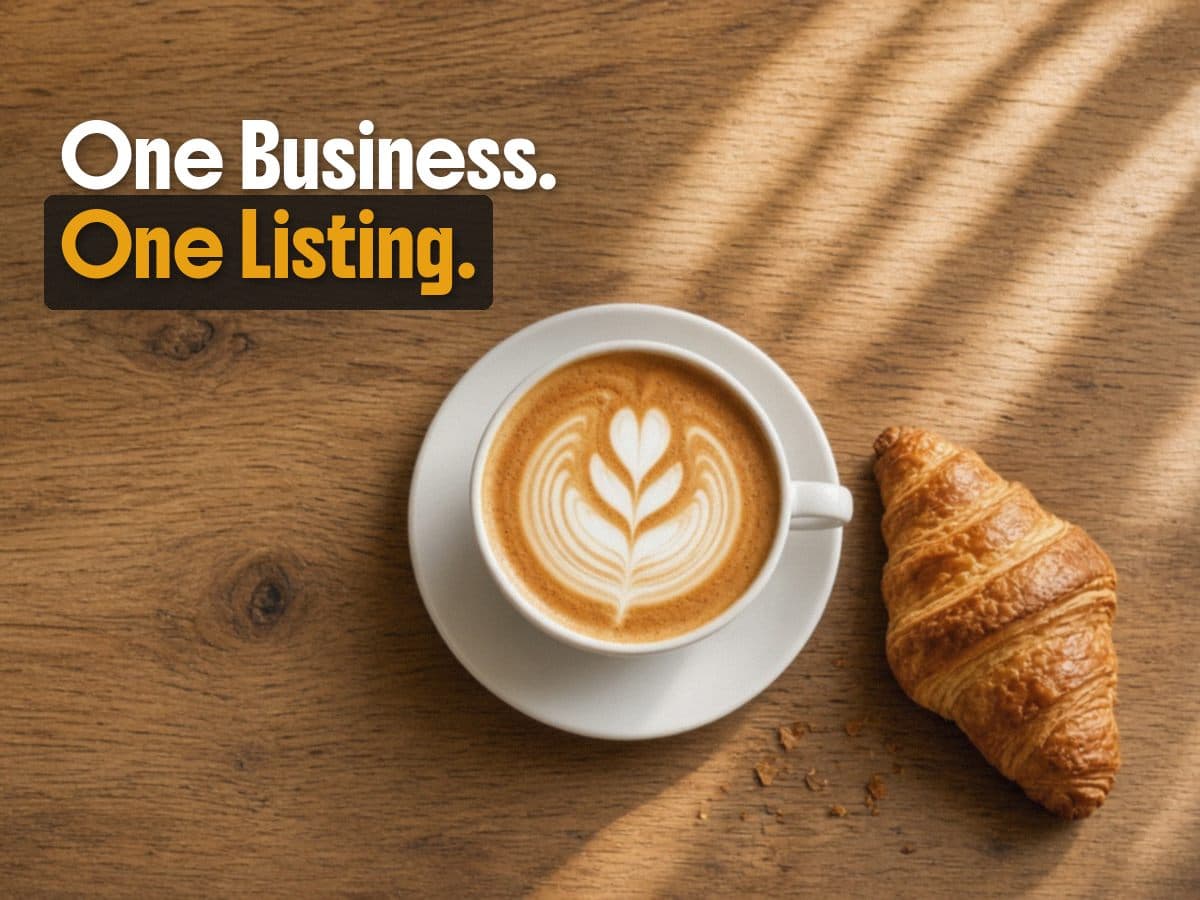 A latte with leaf foam art and a croissant sit on a sunlit wood table, under the words One Business. One Listing.