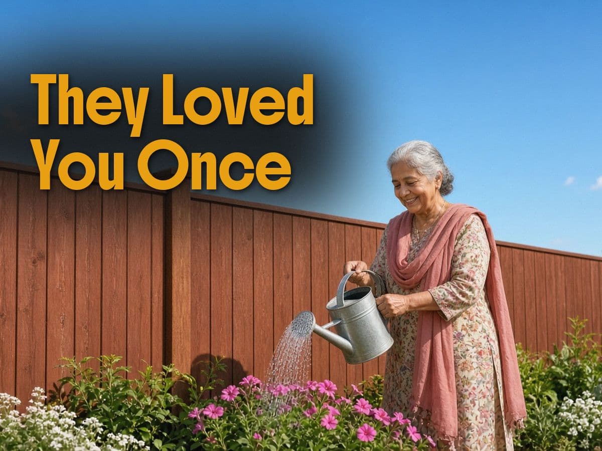 An older woman in a floral dress waters pink flowers with a metal can beside a wood fence, under They Loved You Once.