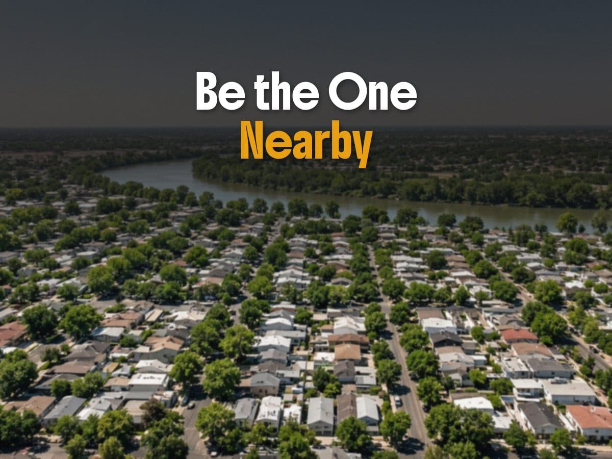 An aerial view of a tree-filled neighborhood along a river, under the words Be the One Nearby.