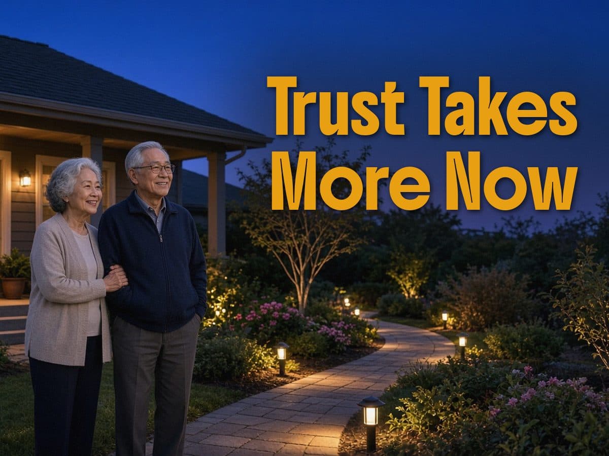 An older couple stands by a lit garden path at dusk, under the words Trust Takes More Now.